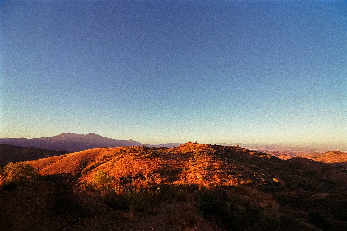 Rolling hills covered in dry vegetation under a clear sky.