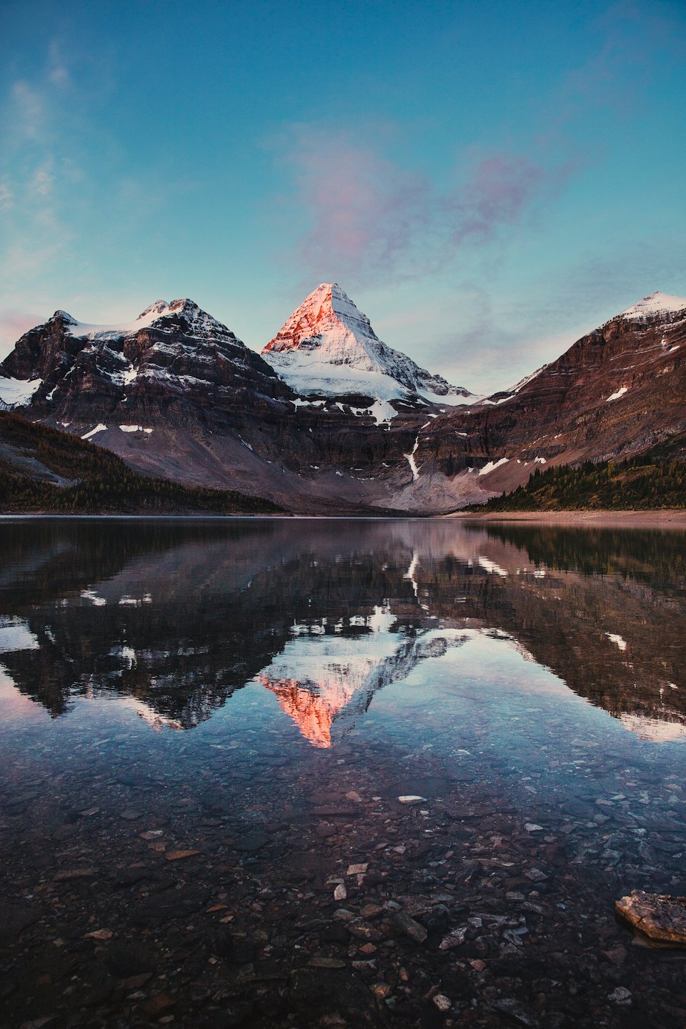 Snow-capped mountain range reflected in a calm lake at sunrise.